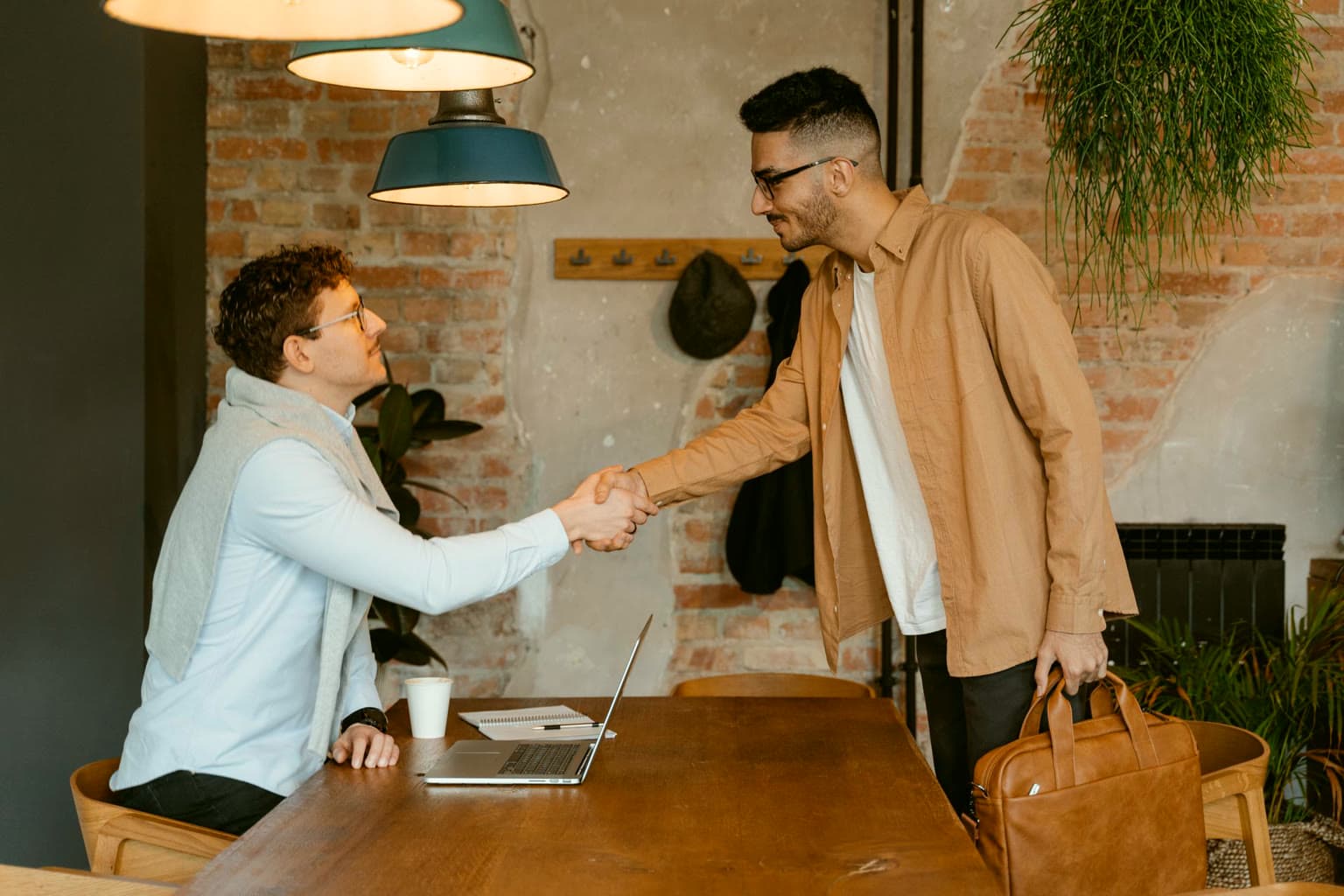 Small-business owner shaking hands with an independent contractor in a brick-walled office