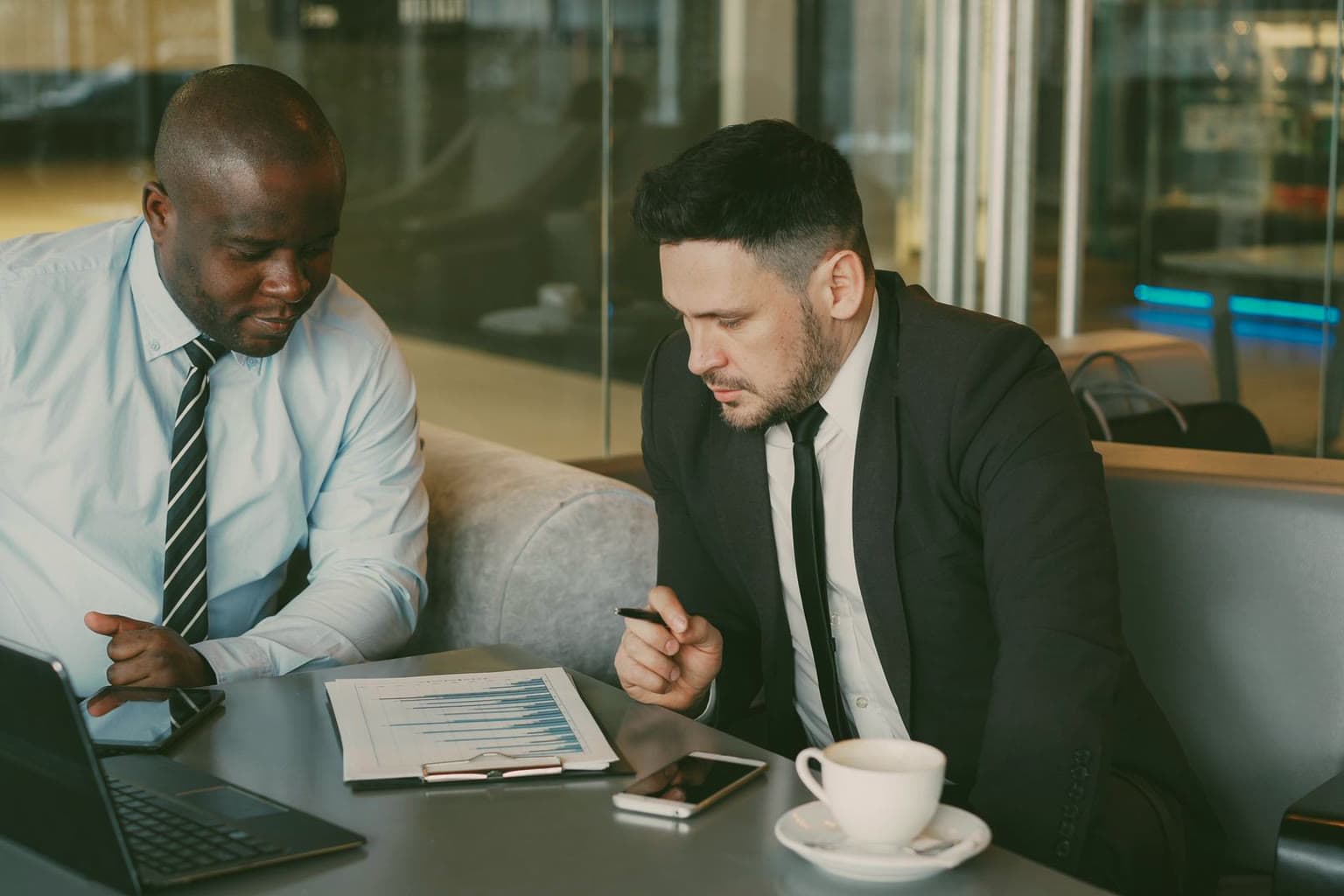Two business owners reviewing a printed financial report with a laptop and coffee