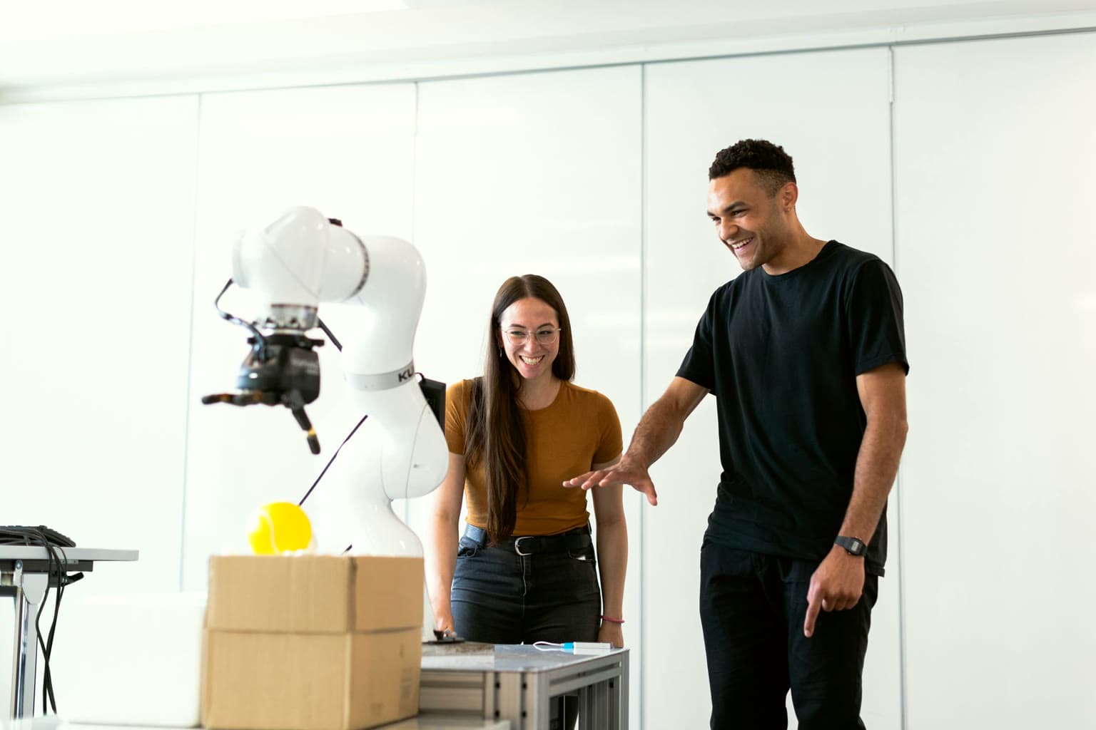 Two engineers testing a robotic arm in a bright workshop