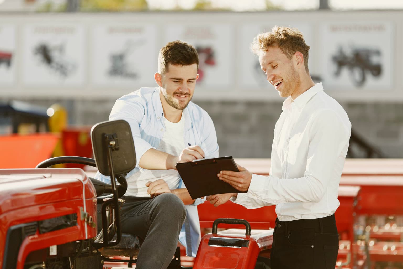 Buyer seated on a new tractor signing purchase paperwork with a dealer