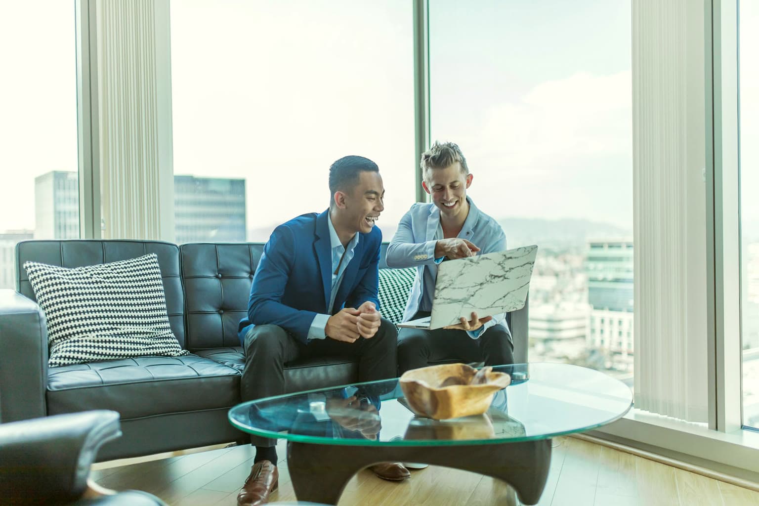 Two co-founders discussing plans on a sofa beside a city-view window