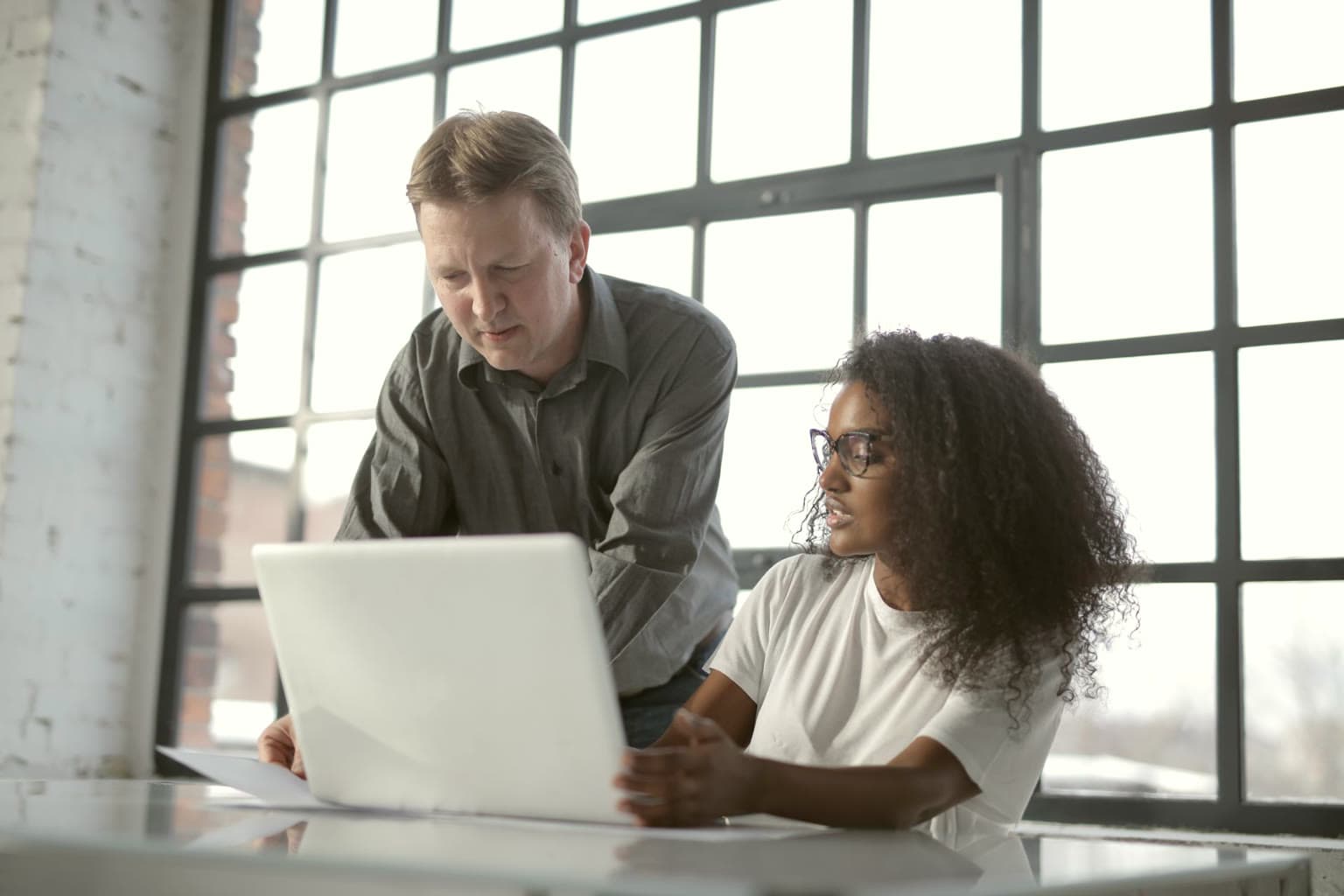 Adviser and business owner reviewing a laptop by large windows