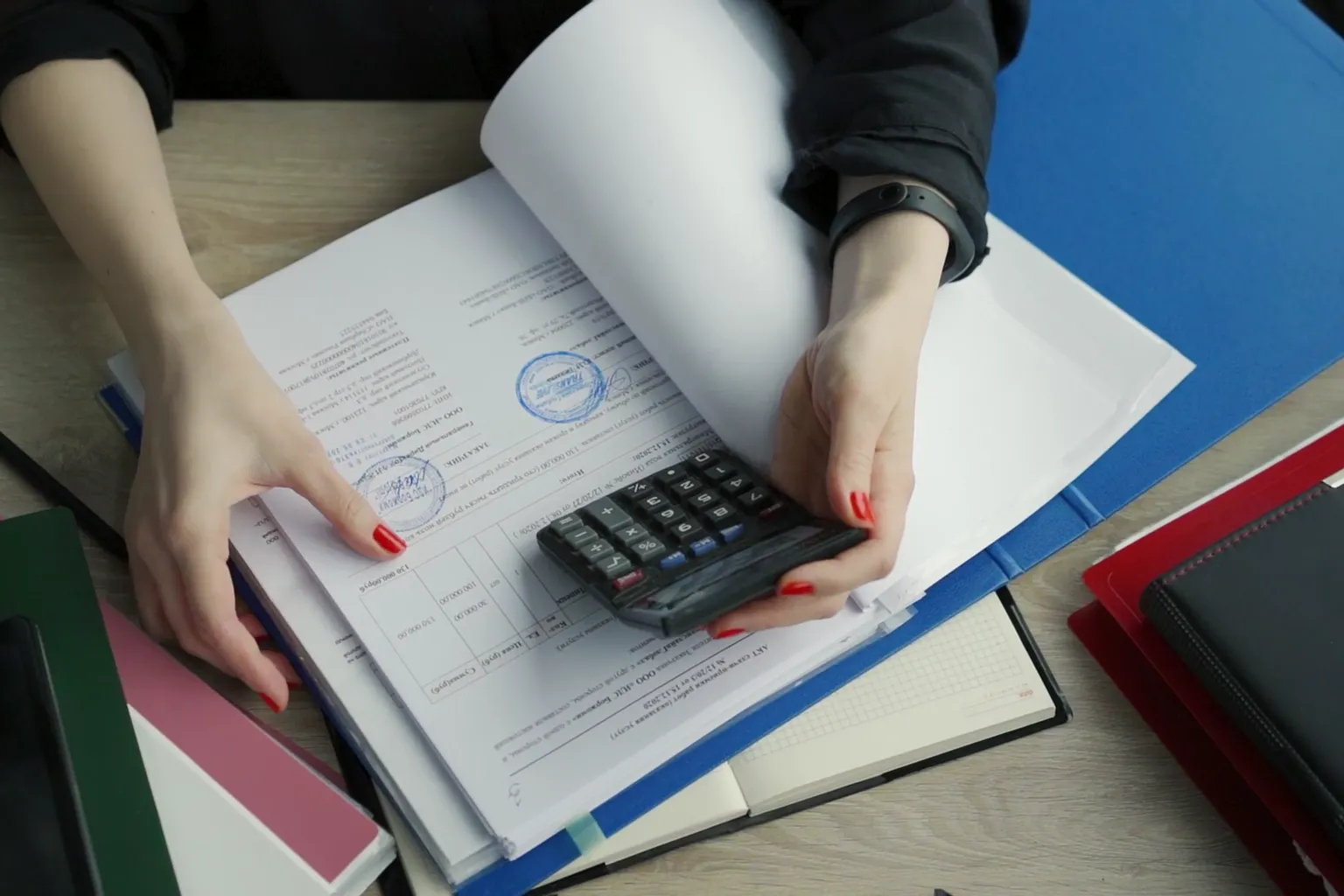 Accountant reviewing bank transfer records, loan statements, and bookkeeping ledgers on a wooden desk